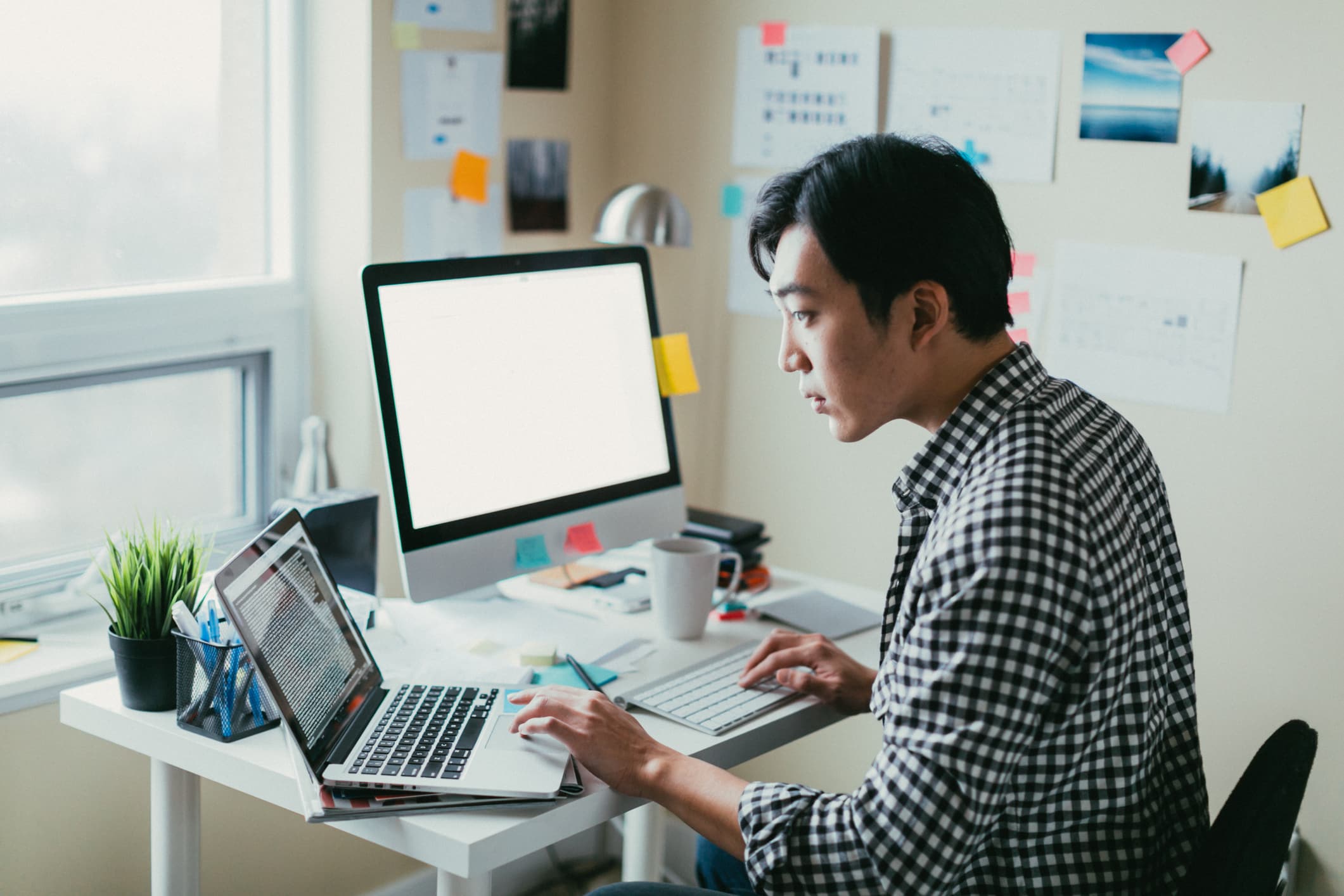 Man looking at computer code on a laptop while working from his small office.