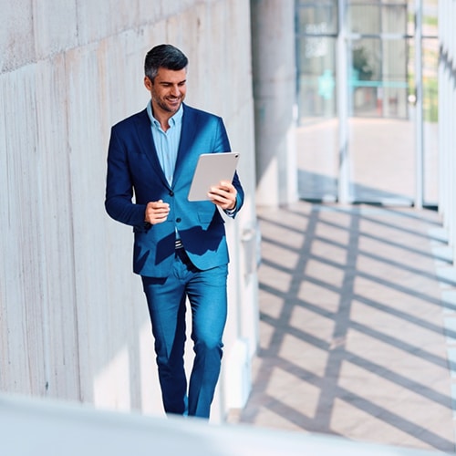 A male professional looking at his tablet while walking