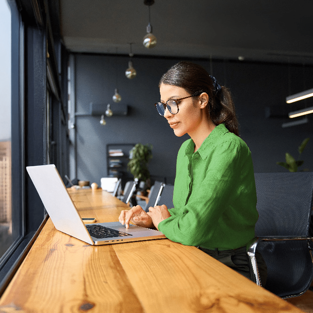 Woman working on a laptop at a long desk.