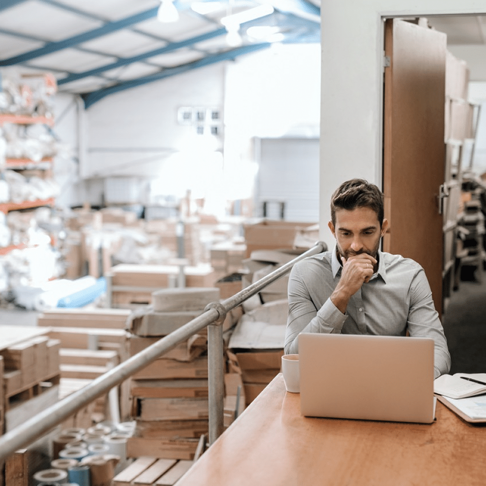 Person working on a laptop at a desk overlooking a busy warehouse
