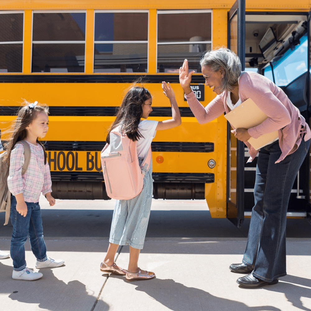 Adult giving a high five to children boarding a school bus