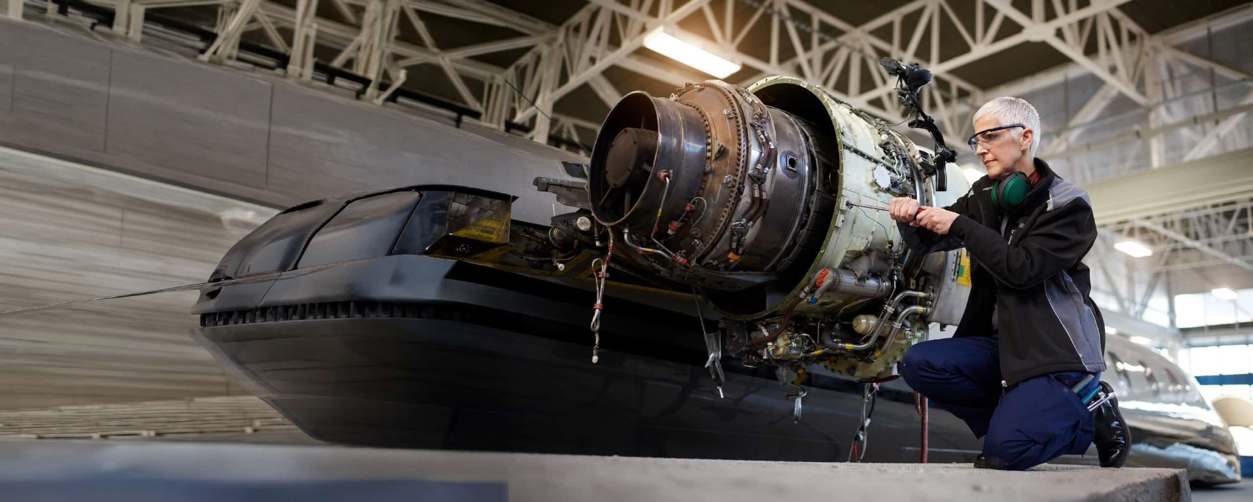 Female technician working on an aircraft engine in a hangar.