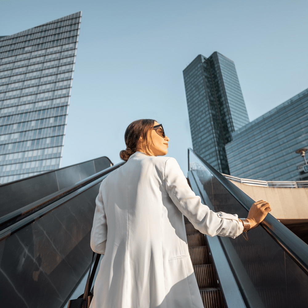 Person riding an outdoor escalator between modern offices.