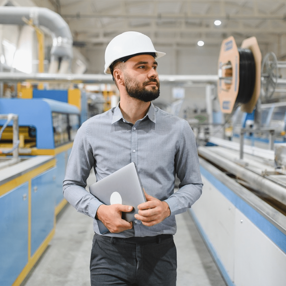 Hard hat wearer carrying a laptop in a factory.
