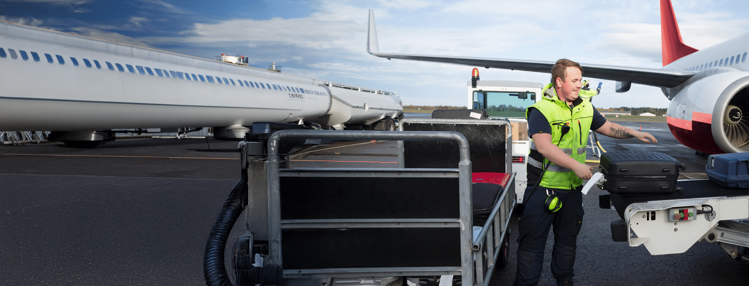 Airport worker loading luggage onto a conveyor belt beside a passenger airplane.