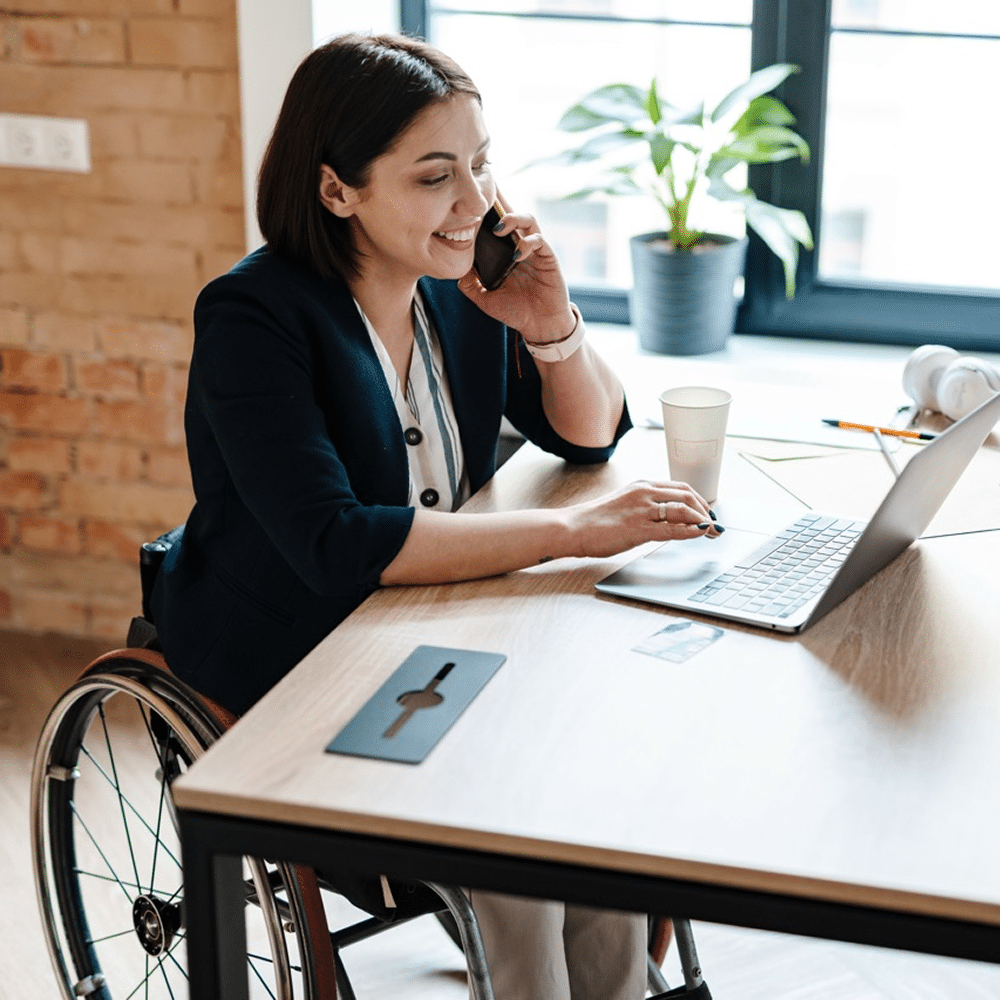 Person in a wheelchair using a laptop and phone.