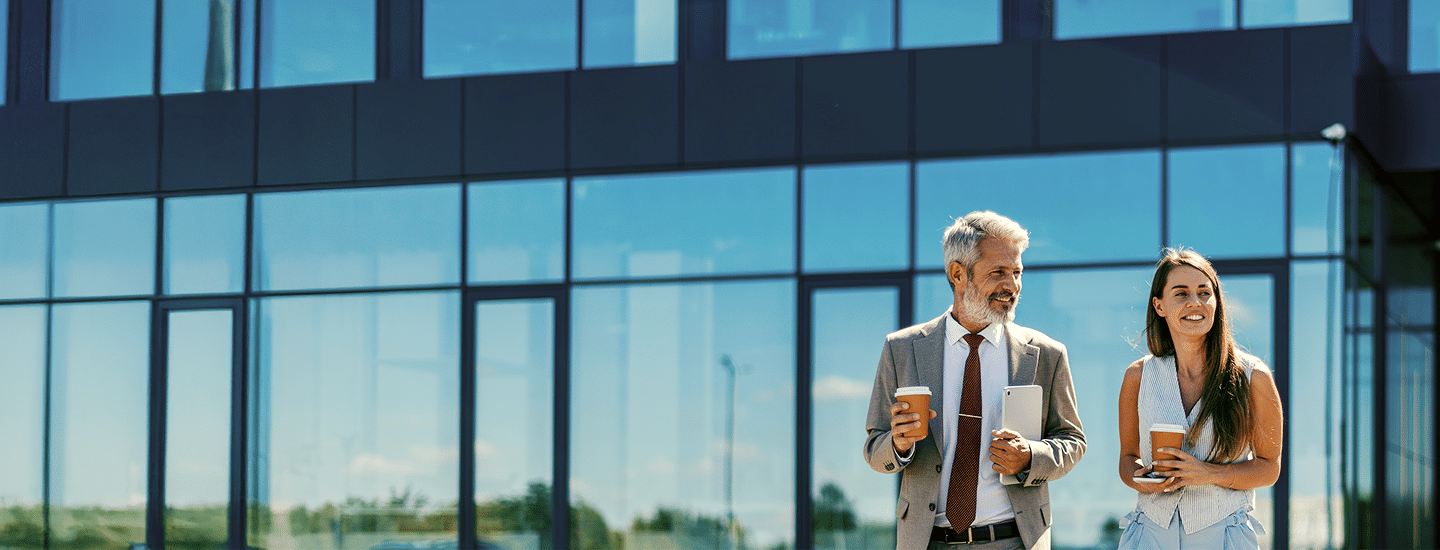 Two professionals holding coffee outside an office.